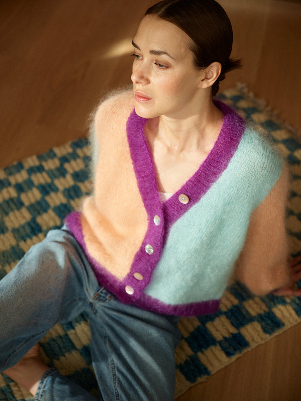 Woman wearing a colorful knitted cardigan sitting on a patterned rug.