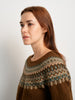 Woman wearing a brown sweater with a patterned neckline against a plain background