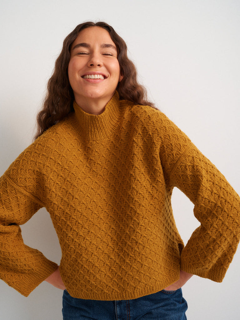 Woman wearing a mustard yellow sweater against a white background