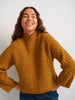 Woman wearing a mustard yellow sweater against a white background