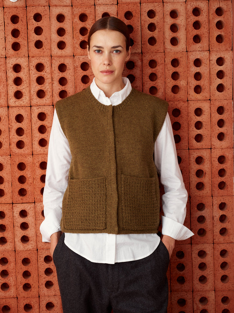 Person wearing a brown vest over a white shirt against a brick wall.
