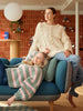 Two women sitting on a blue couch with a striped blanket, in a room with a brick wall.