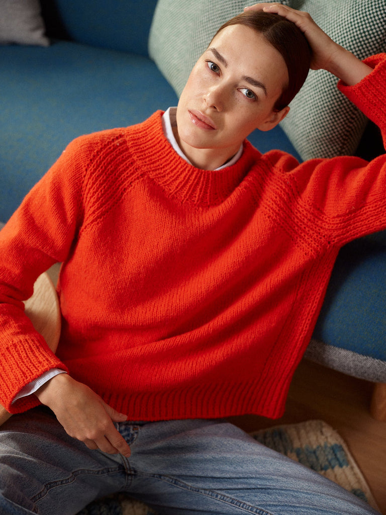 Person wearing a red sweater sitting on a blue couch.
