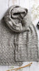 Knitted gray scarf on a wooden surface with knitting needles and flowers.