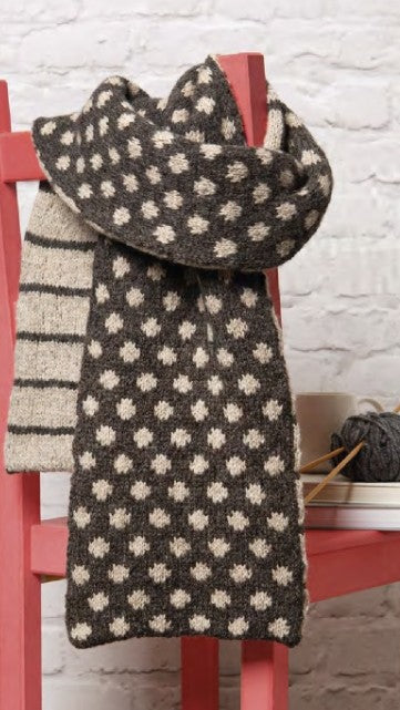 Knitted scarf with a pattern draped over a red chair against a white brick wall.