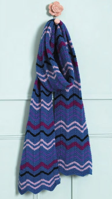 Colorful knitted scarf with zigzag pattern hanging on a hook against a light blue wall.