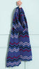 Colorful knitted scarf with zigzag pattern hanging on a hook against a light blue wall.