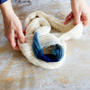Person holding a skein of yarn with blue and white colors on a wooden surface