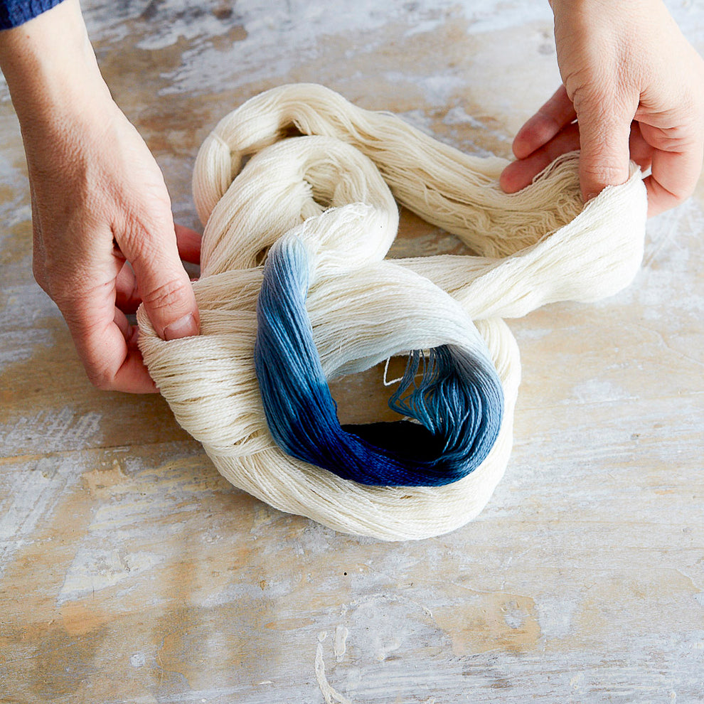 Person holding a skein of yarn with blue and white colors on a wooden surface