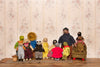 A group of handmade plush teddy bear figures and animal characters posed together on a wooden surface against a vintage floral wallpaper background.