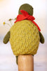 A close-up back view of a knitted turtle doll wearing a red scarf, mounted on a wooden stand against a soft light background.