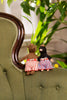 Two small knitted teddy bears wearing striped shorts sit on the back of an olive green tufted armchair, with a blurred indoor plant in the background.