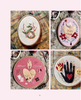A collage of four oval and round embroidered art pieces displayed on a distressed painted wood surface, with small sewing tools around them. The designs include a green snake on cream, a pink heart with flowers and the words 'in love', a pink heart with 'amor eterno' on dusty pink, and a black hand with a red heart and small sun on cream.
