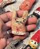 Hand holding a small embroidered cat figurine with colorful patterns on a textured surface.