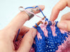 Close-up of hands knitting with blue and pink yarn on wooden needles.