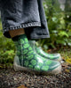 Person wearing transparent rain boots with green pattern and jeans in a natural setting