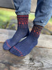 Blue socks with red patterns worn by a person sitting on a wooden surface.