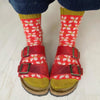 Red sandals with buckles worn with red and white patterned socks on a light wooden floor.