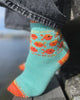 Teal sock with orange fish pattern worn by a person by a body of water.