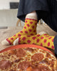 Person wearing yellow socks with red polka dots sitting on a pizza.