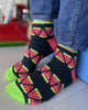 Person wearing black socks with red and green watermelon pattern on a light wooden floor.