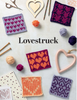 A flat lay of knitted heart-pattern swatches in multiple colors, arranged with knitting needles, yarn balls, scissors, wooden heart ornaments, and patterned paper on a light background. The word 'Lovestruck' is printed in the center.