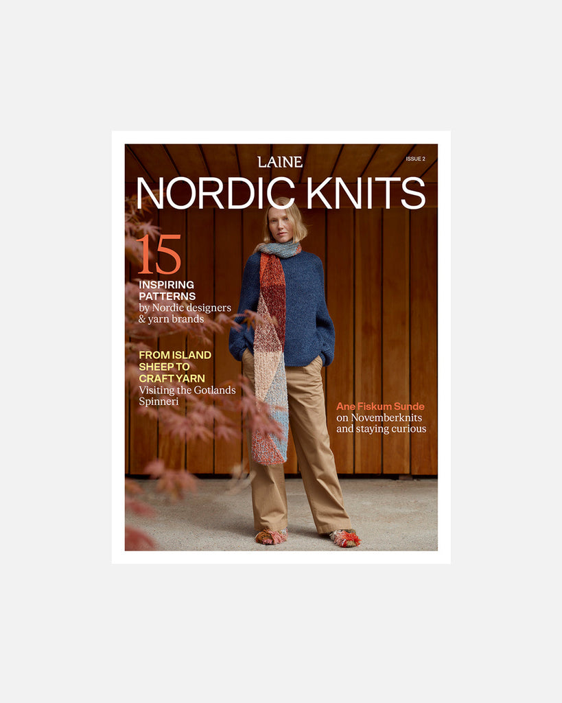 A book or magazine cover titled 'Laine Nordic Knits' featuring a woman standing in front of a wooden wall, wearing a blue sweater, tan pants, and a long multicolored scarf. The cover includes text about patterns and knitting inspiration.
