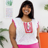 Woman wearing a white crochet top with colorful patterns in a home setting