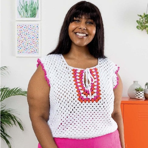Woman wearing a white crochet top with colorful patterns in a home setting