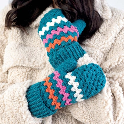 Pair of teal mittens with colorful pattern on a textured beige surface