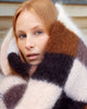 A close-up of a woman wrapped in a fuzzy, oversized knit blanket with large checkered blocks of cream, brown, and dark charcoal.