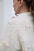 Close-up of a woman wearing a chunky cream knit sweater with pom-pom details and small pastel accents, paired with large gold hoop earrings.