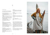 Woman standing by a lake with a tree stump, wearing a yellow cardigan and white dress.