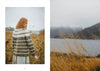 Person in a striped sweater standing in a field with a lake and mountains in the background
