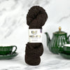 Dark brown yarn skein with a label on a marble surface with green teacup and teapot in the background.