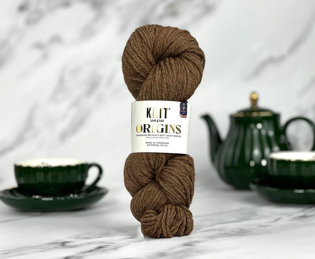 Brown yarn skein with a label on a marble surface with a teacup and teapot in the background.
