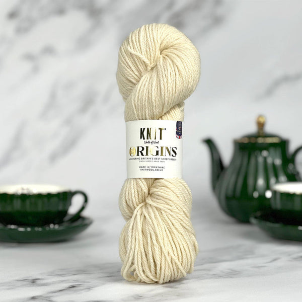 Ball of cream yarn with a label on a marble surface with a green teapot and cup in the background.