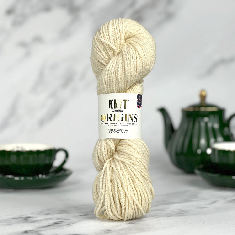 Ball of cream yarn with a label on a marble surface with a green teapot and cup in the background.