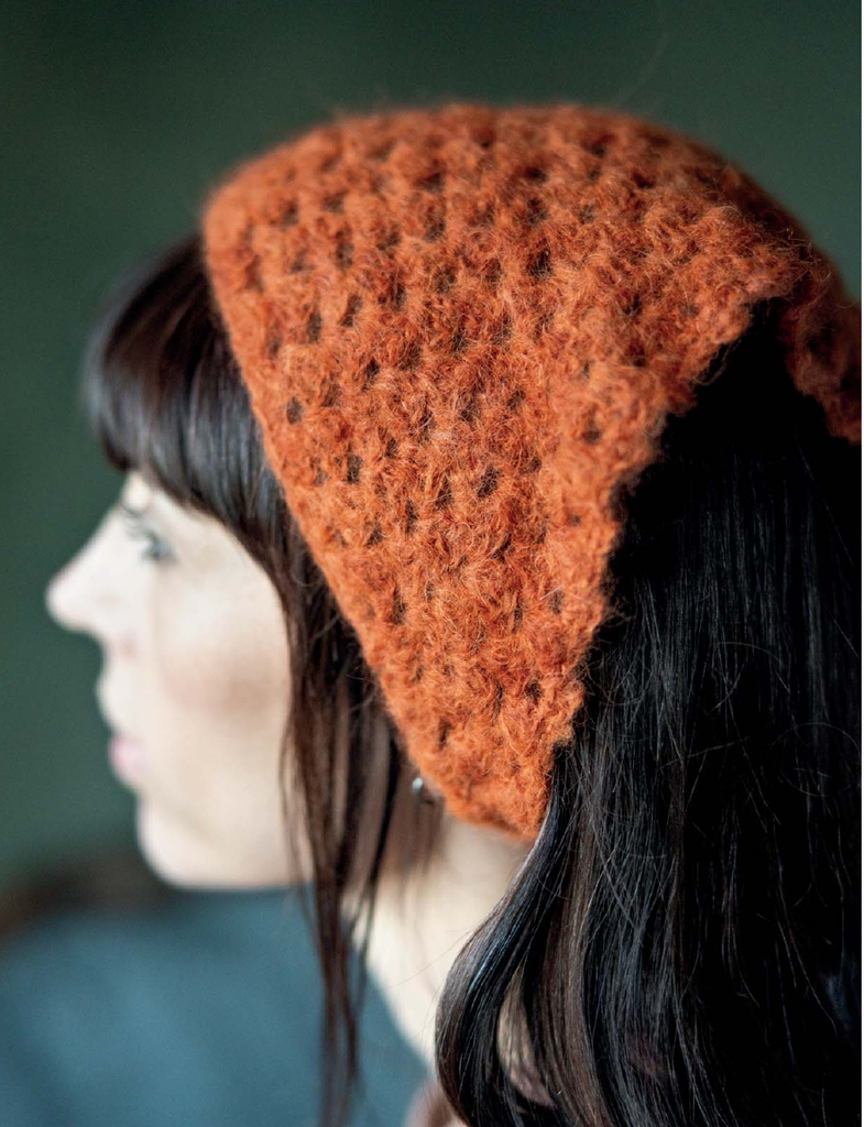 A close-up side profile of a woman wearing a fuzzy, textured burnt orange knit bonnet or head covering against a dark green background.