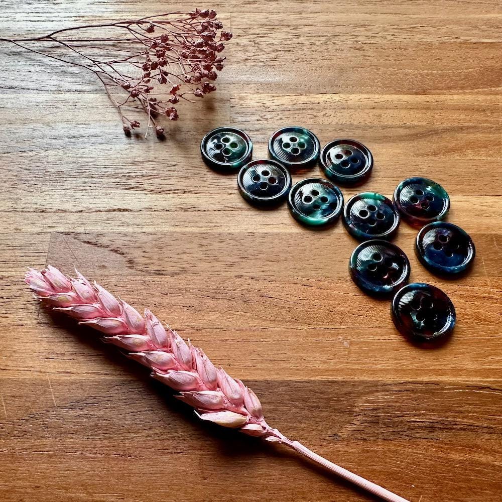 Black buttons arranged on a wooden surface with dried pink flowers.