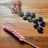 Black buttons arranged on a wooden surface with dried pink flowers.