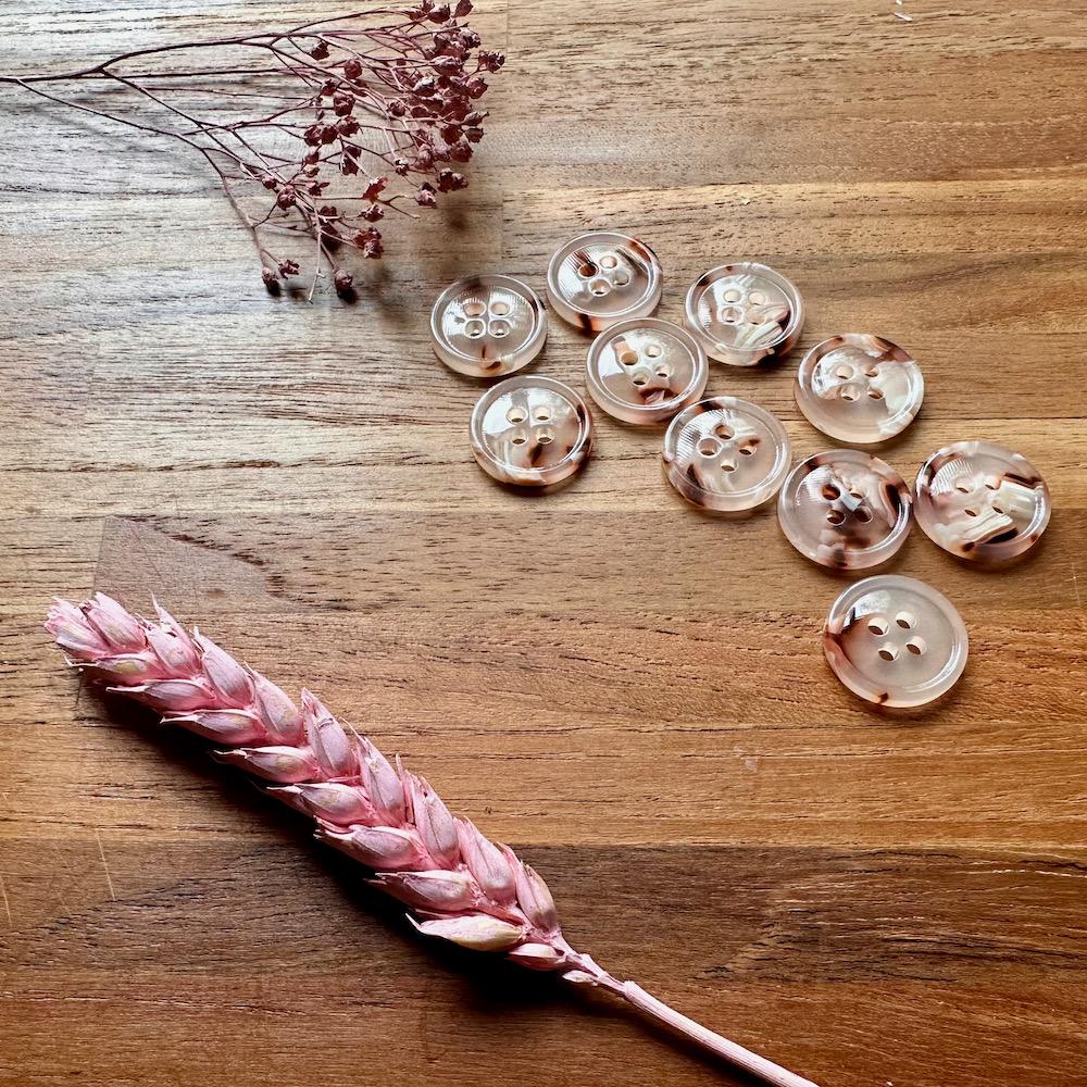 Clear buttons with floral patterns on a wooden surface with dried pink flowers.