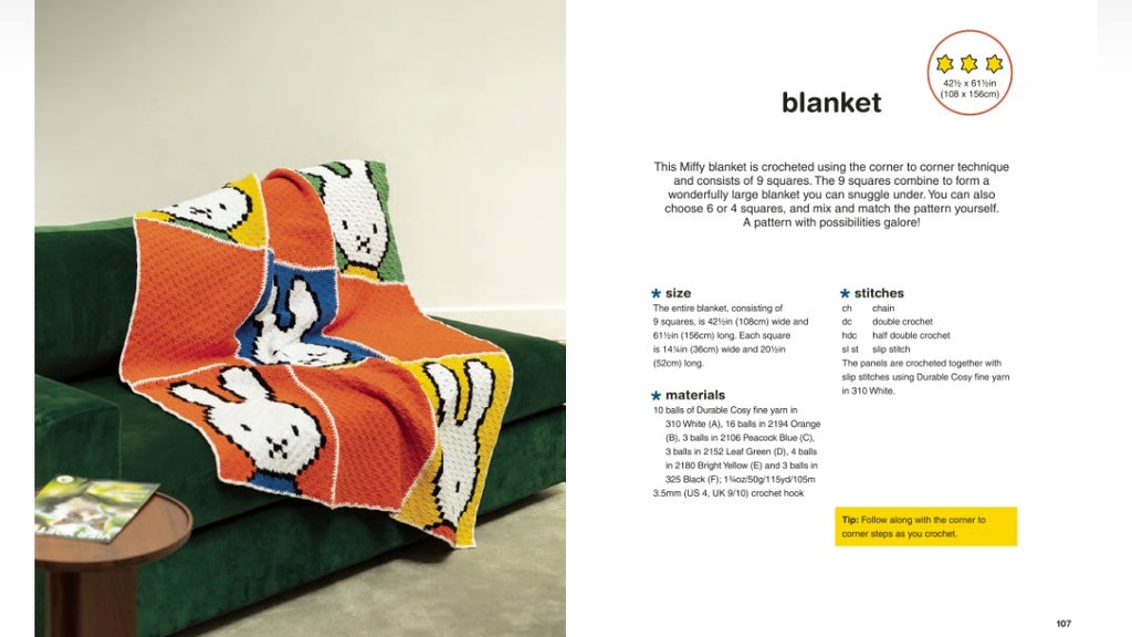 An open book showing a crochet blanket pattern page. The left page features a photo of a colorful crocheted blanket draped over a green chair, with the right page containing the title 'blanket', a star rating, dimensions, stitch count, materials, and instructions.