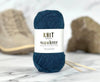 Blue yarn ball with 'Knit Wanderer' label on a marble surface with knitting needles.