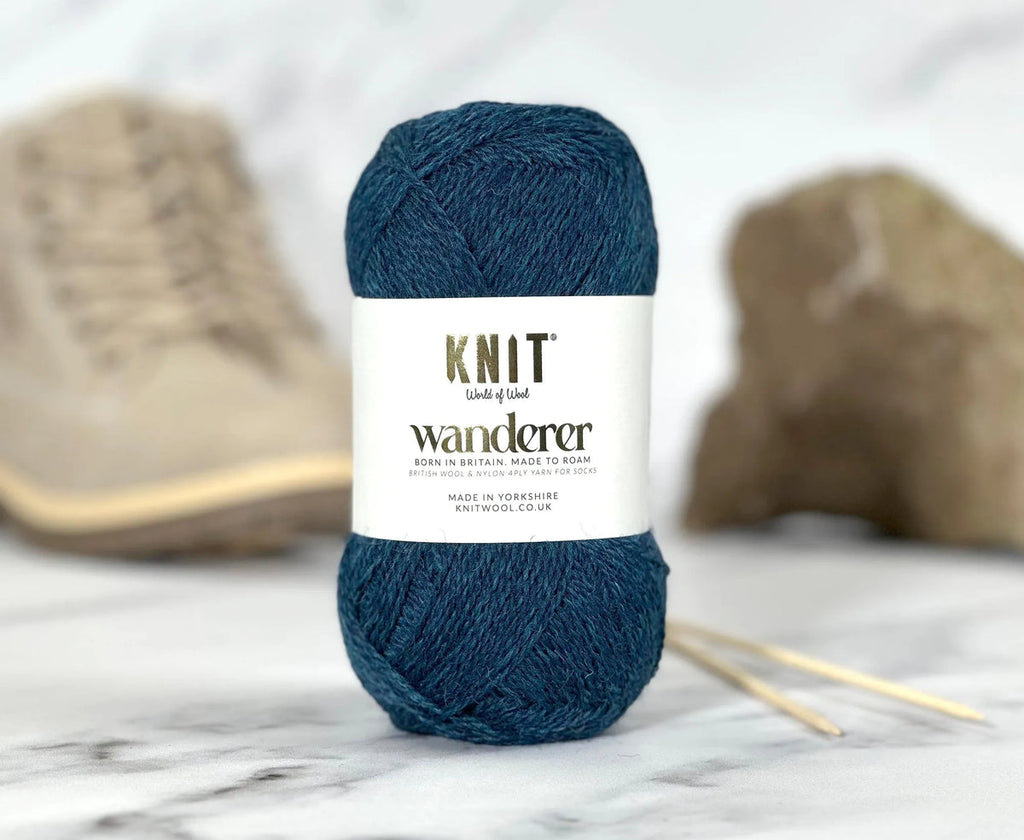 Blue yarn ball with 'Knit Wanderer' label on a marble surface with knitting needles.