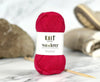 A skein of bright pink yarn with a white label reading 'KNIT lives of knit wanderer' is centered on a marble surface with knitting needles and soft blurred background props.