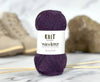 Ball of purple yarn with 'Knit Wanderer' label on a marble surface