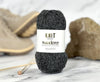 Ball of yarn with a label on a marble surface with knitting needles and stones in the background