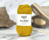 Yellow yarn ball with 'Knit Wanderer' label on a marble surface with knitting needles.