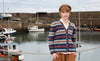 Woman wearing a patterned cardigan standing by a harbor with boats.